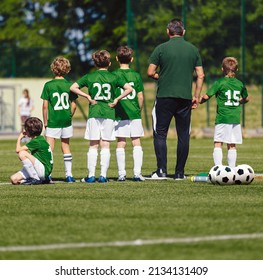 Square Photo Of Young Boys And Soccer Coach Watching A Football Match. Youth Reserve Substitute Players Ready To Play The Tournament Match. School Soccer Team In Green Jerseys With Trainer