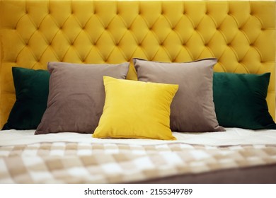 Square pillows of various colors and sizes lie on the bed with a soft yellow velvet headboard with capitones. Selective focus.