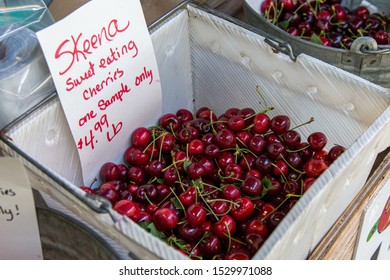 A Square Plastic Bucket With Red Cherries At A Farmers Market. A White Price Tag Read 