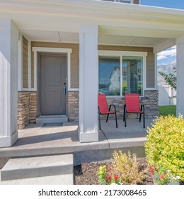 Square Porch Of A Two-storey House With Red Armchairs And Front Garden. Entrance Of A House With Light Brown Front Door With Lockbox Near The Garage With White Sectional Door.