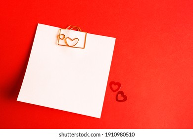 Square sheet for notes with a paper clip in shape of a letter and a heart. Decor of couples in love with hearts on a red background. Valentine's Day, message, greeting, declaration of love. Copy space