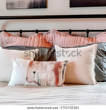 Square Single bed with fluffy pillows against black metal headboard inside bedroom