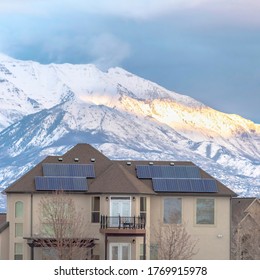 Square Solar Panels On Roof Of Home With Lake And Snowy Mountain Background In Winter