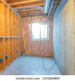 Square Sun Flare Unfinished Food Storage Room At The Basement With Window. Empty Basement Interior With Wood Frames And Panel On The Left Across The Concrete Wall On The Right.