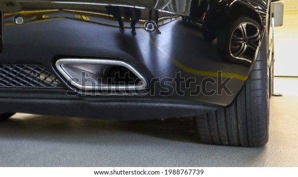 Square tailpipe at the rear right\
side of a black sports car. Very low plan. The rear bumper, wheel\
and tailpipe of the packed vehicle are smoke- and\
gas-free