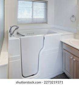 Square Walk-in bathtub with elderly and handicapped accessibility. There is a vanity sink with mirrors on the right and shower stall with frosted glass and aluminum frames. - Shutterstock ID 2273219371