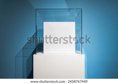 Square white box mockups inside blank glass box podium mockup in exhibition gallery. Empty showcase mock up. Clear exhibition cube for museum or store. Display cabinet for expo.