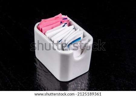 A square white ceramic restaurant sugar and sweetener packet holder on a black table with reflection