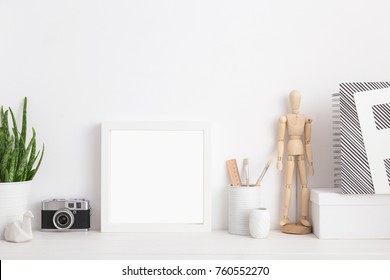 Square white frame mock up. Creative desk with blank picture frame or poster, wooden mannequin, camera desk objects, artist supplies and plant on a white background.  - Powered by Shutterstock