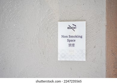 Square white paper no smoking sign on a wall in public place. No smoking sign is black line crossed cigarette smoke with English and Chinese letter means, No Smoking. - Shutterstock ID 2247235565