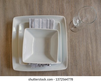 Square white plates of place setting with water glass on grey wood table. Interior design element for dining room.  Clean white ceramic dishes.  - Powered by Shutterstock