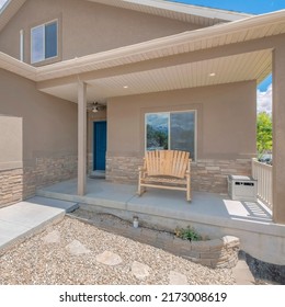 Square White Puffy Clouds Exterior Of A Light Brown Two-storey House With Garage. Facade Of A House With Wooden Bench And Blue Front Door On The Porch At The Left Beside The Garage With White Door