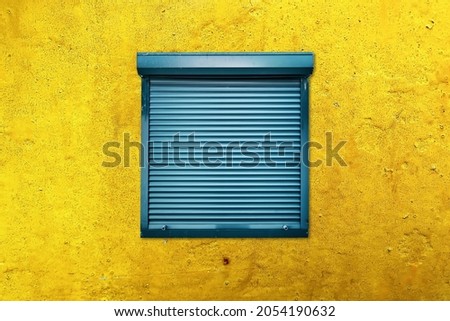 Square window with closed blue blinds or rolling shutter on a yellow weathered wall. Secrecy, mystery or protection concept.