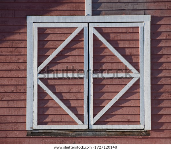 square window frame in white wood\
divided into triangles on side of red barn in sun with rigid\
shadows on sunny day in rural area horizontal format\
