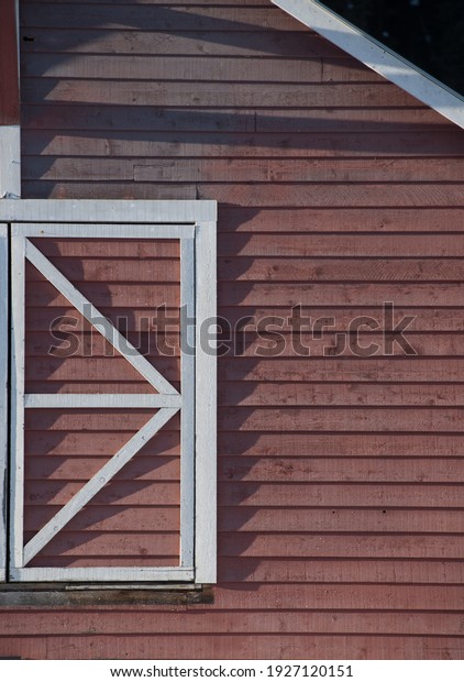 square window frame in white wood divided into\
triangles on side of red barn in sun with rigid shadows on sunny\
day in rural area vertical format\
