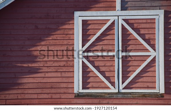 square window frame in white wood\
divided into triangles on side of red barn in sun with rigid\
shadows on sunny day in rural area horizontal format\
