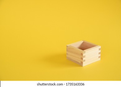 Square wooden measuring cup on yellow background.