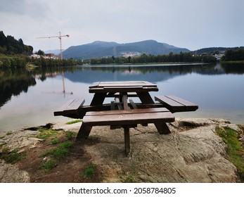 A Square Wooden Table With Benches Around It Overlooking A Tranquil Lake On A Beautiful Day Outside