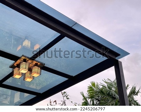 A squared lamp hanging on a steel structure of a translucent sheet roof.