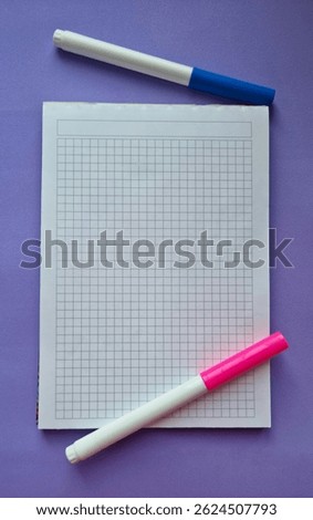 Squared school notebook with pink and blue felt-tip pens on purple background. Flat lay vertical composition with copy space. Back to school and education concept