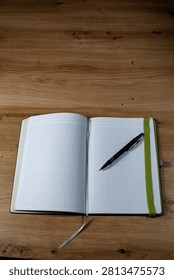 Squared side in a notebook with a dark and silver ballpen and a green rubberband on a wooden table.