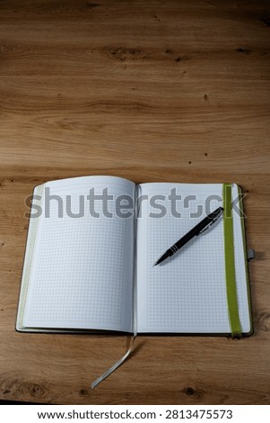 Squared side in a notebook with a dark and silver ballpen and a green rubberband on a wooden table.