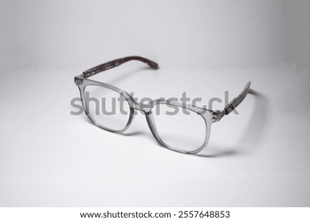 Square-shaped glasses with a gray frame accompanied by a unique wooden pattern facing left isolated on a white background. Minimalist glasses display with copy space for text with 45 degree shot.