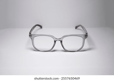 Square-shaped glasses with gray frames accompanied by a unique wooden pattern facing forward isolated on a white background. Minimalist glasses display with copy space for text with 45 degree shot.