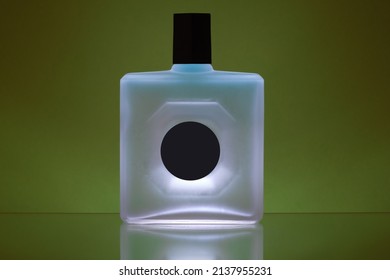 Square-shaped Perfume Bottle With Opaque Glass Is Resting On A Glossy Plane, The Background Is Backlit With Green Light, The Black Label Does Not Bear Any Brand.