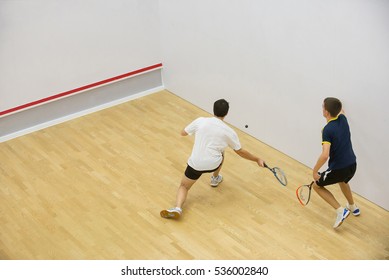 Squash players in action on squash court, back view/Two men playing match of squash.
