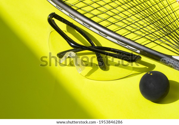 Squash racket, ball and\
glasses on a bright yellow background. Squash sport equipment in\
trendy style.