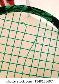 Squash racket with torn string with squash court at the background