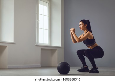 Squat exercises. Girl in black sportswear with dumbbells in her hands doing squats in a room.