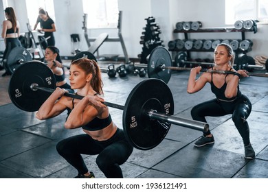 Squats With Barbell. Group Of Young Sportive People Indoors In Gym.