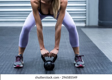 Squatting muscular woman lifting kettlebells at the crossfit gym