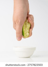 Squeezed lime isolated, hand squeezing out half green lemon, squeezed lime juice on white background, burnout symbol, making a Cuba Libre cocktail