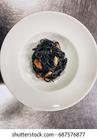 squid ink tagliolini, sweet garlic cream and mussels in a round white plate 