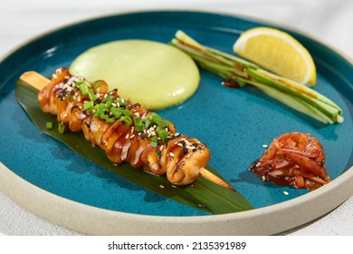 Squid yakitori in ceramic dish on white background. Japanese skewered squid with wasabi sauce. Grilled kalmar on bamboo skewer in asian style. Food menu for izakaya. Summer pan asian menu