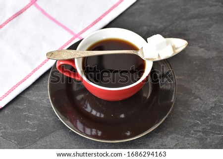 A squiggled teaspoon lies on a red coffee cup with three pieces of sugar on top - concept for enjoying coffee as a relaxing ritual during the day