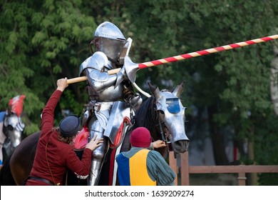 Squires help equip a knight in plate armor on a horse. Knight with a knight's spear.