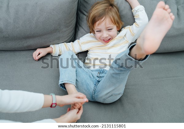 Squirming laughing boy being foot-tickled on the\
couch by girl\'s\
hands.