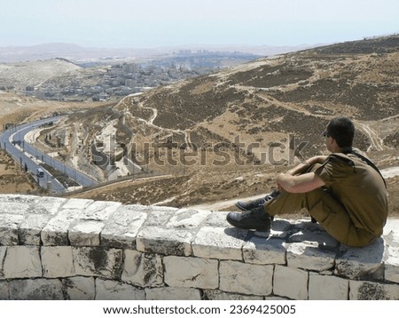 sraeli soldier sitting on a wall overlooking the area near Jerusalem