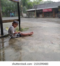 Sragen, March 3, 2022 - A Small Child Playing In The Rain Alone On The Side Of The Road