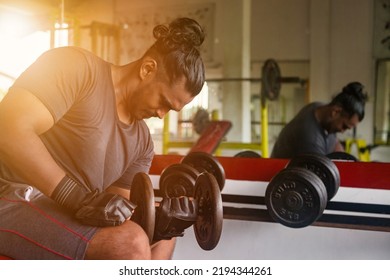 Sri Lankan Bodybuilder Man Sitting And Lifting Dumbbell At Mirror. Sportsman Doing Exercises With Dumbbells At Old Gym. Athletic Asian Man Pumping Up Muscles Workout. Sports And Bodybuilding Concept