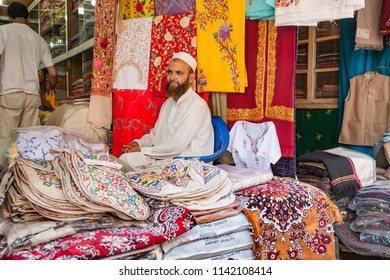 Srinagar ,23 June,2008:Portrait Of   Muslim Shop Keeper In White Clothes,
With Beard And Cap,sitting In Ready Made Cloth Shop  Against  Colorful Embroidery Textiles Background, Jammu And Kashmir,India