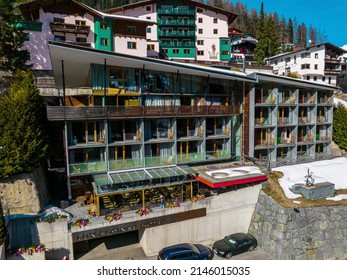 St. Anton am Arlberg. March 10, 2022. Luxurious hotel lux alpine against forest in town. High angle view of cars parked outside ski resort . Beautiful vacation home in alpine region during winter.
