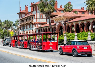 St. Augustine, USA - May 10, 2018: Flagler College With Florida Architecture, Famous Statue In Historic City, And Red Train Trolley Tour Guide Tram