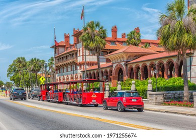 St. Augustine, USA - May 10, 2018: Flagler College With Florida Architecture In Historic City And Red Train Trolley Tour Guide Tram Riding On Street Road For Tourists