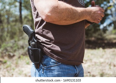 St. Jo, Texas / USA - March 28, 2020: Close up side view of a man wearing an open carry handgun in a holster at his belt outdoors 