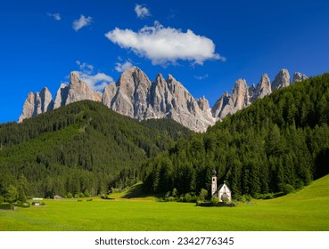 St Johann Church with landscape view of dolomites mountain peaks and blue sky, Santa Magdalena alpine village, Italy